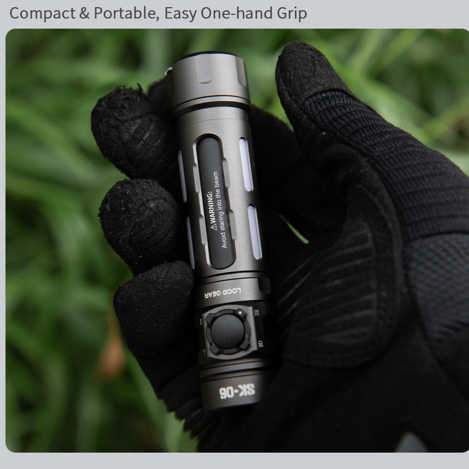 A black tactical flashlight with a textured grip and silver accents, held in a hand wearing a black glove against a blurred green background. Text at the top reads 'Compact & Portable, Easy One-hand Grip'.